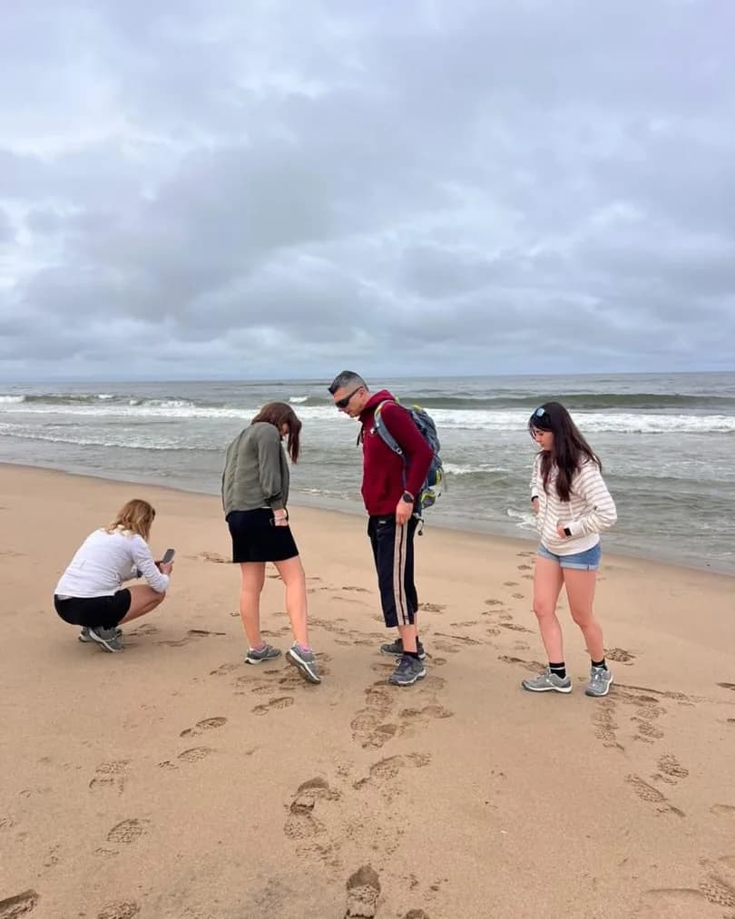 Four guests walking a wide Atlantic beach, one crouching to photograph footprints in the sand