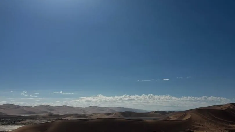 The sun bursting over dunes above a thin sheet of water on the sand