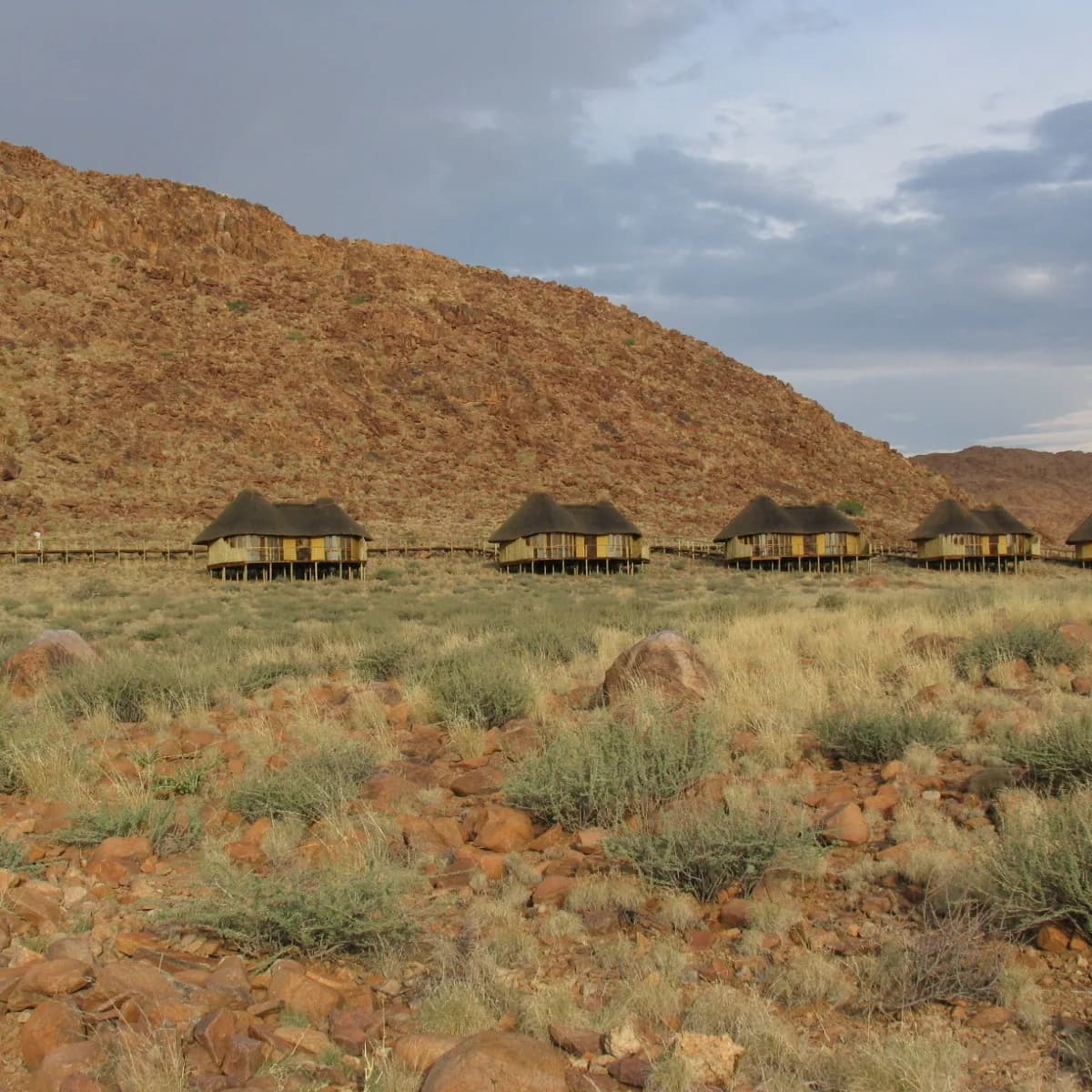Row of thatched chalets on stilts below a rocky red hillside