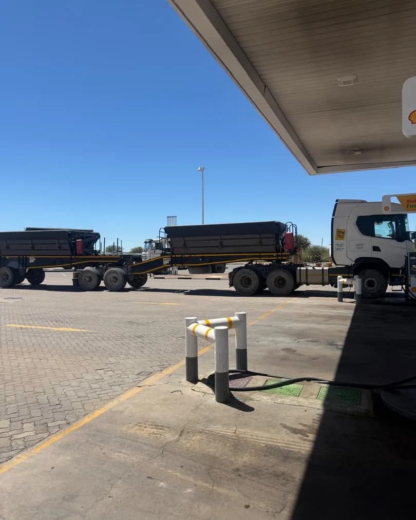 Haul trucks parked in a line at a desert road stop under a canopy roof