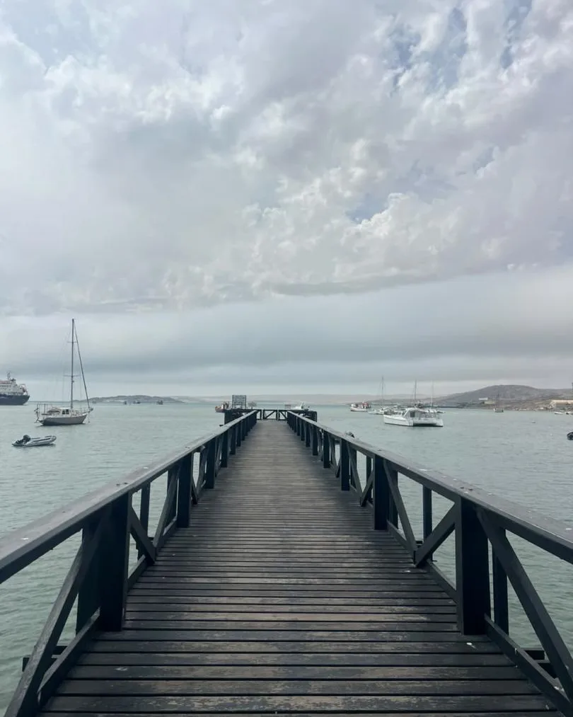 A long wooden jetty reaching into calm Atlantic water, sailboats moored in the bay